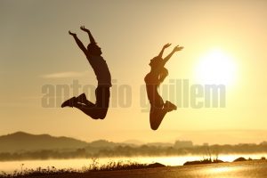 Fitness couple jumping happy at sunset with the sun in the background