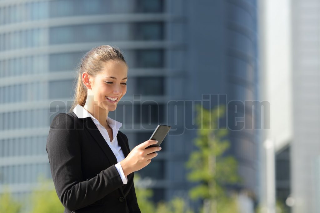 Executive working with a mobile phone in the street with office buildings in the background