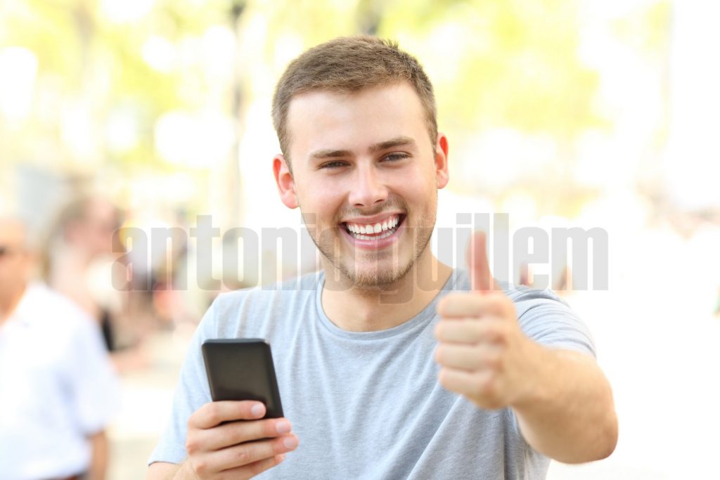 Man with thumbs up holding phone looking at you
