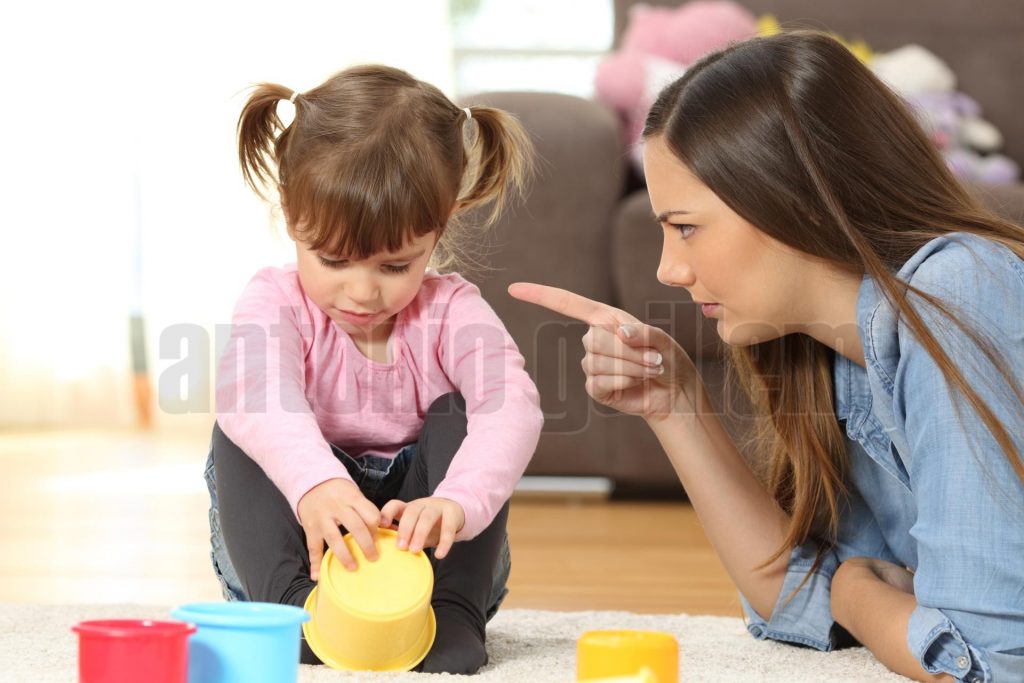 Portrait of a mother scolding to her baby daughter sitting on the floor in the living room at home