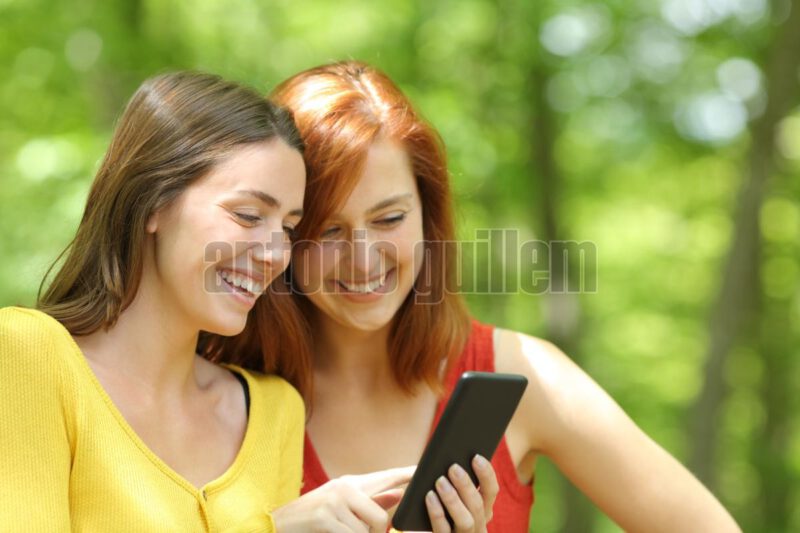 Two happy women checking smart phone in a forest