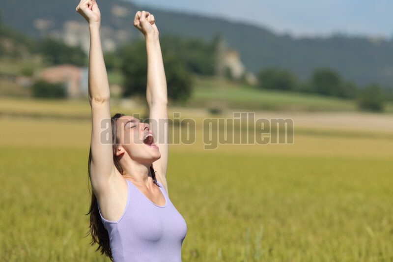 Excited woman raising arms celebrating in a wheat field